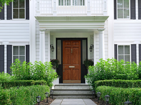 House with white siding and elegant portico entrance and wood grain front door