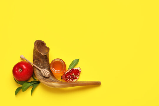 Jar of sweet honey with ripe apple, pomegranate, plant leaves and shofar on yellow background. Rosh hashanah (Jewish New Year) celebration