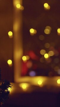 Vertical video. Close Up of a Decorated Christmas Tree With Warm Golden Lights and Window Reflections of a Fireplace, Cozy Holiday Atmosphere, Shallow Depth of Field and Winter Evening