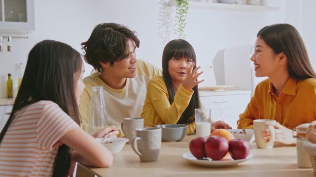 Smiling Multiracial Family Of Four Including Two Children, Enjoying Meal And Sharing Laughter Around Kitchen Table At Home, Creating Cheerful Moments And Strengthening Family Bonds.