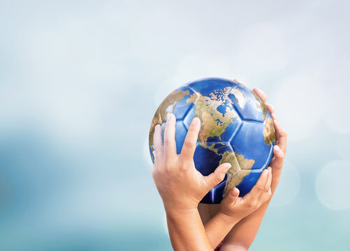 Hands holding planet earth globe soccer ball on soft blue bokeh background for global sports and peace concept design