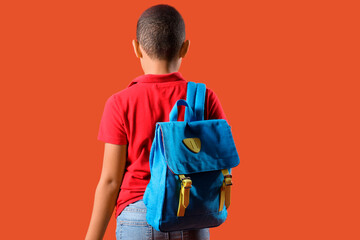 Obraz premium Little schoolboy with backpack on orange background, back view