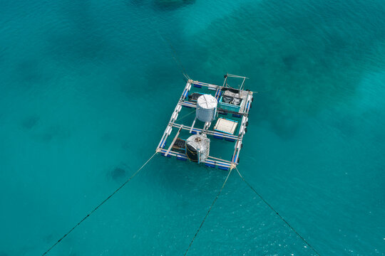 Aerial view of a floating aquaculture platform with storage tanks and equipment anchored in the clear turquoise waters of the Indian Ocean in Makunudhoo, Haa Dhaalu Atoll, Maldives.