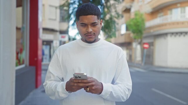 Man with beard holding smartphone in both hands, looking up from screen on urban street; calm reflection.