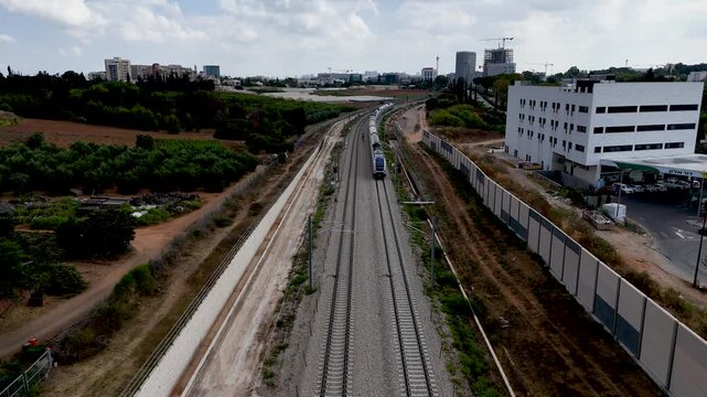 Cinematic Drone Hover Facing North as Passenger Train Approaches and Passes Beneath, Railway Tracks on Western Border of Rehovot Israel, Dynamic Aerial Transport Footage