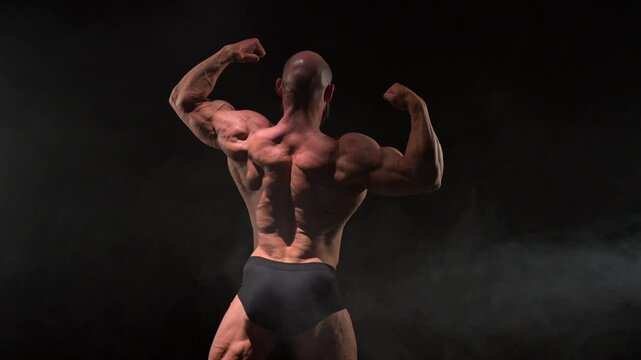 A male bodybuilder poses in shorts, showing off his back muscles.