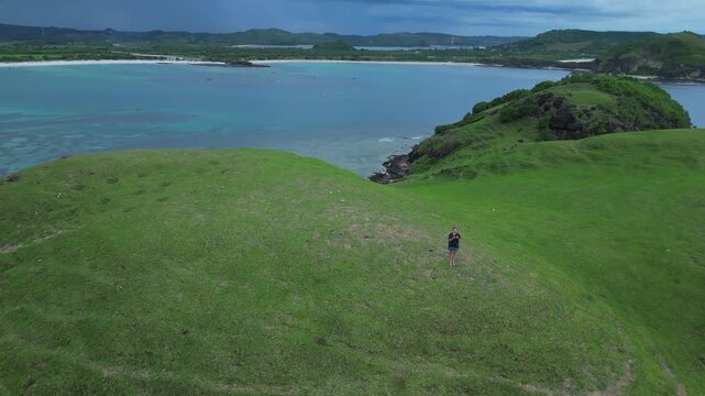 Woman Walking Toward Cliffside Ocean Viewpoint With Sweeping Sea Horizon Empty Grassy Plateau, Rocky Outcrops, Calm Water Tones, Cinematic Aerial Reveal Emphasizing Remoteness, Lombok island