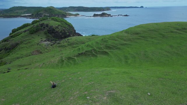 Woman Resting On Hilltop Overlooking Turquoise Bay And Narrow Headland Seated Figure Gazes At Calm Water, Soft Light,Aerial Composition Evokes Peace And Contemplation, Bukit Merese,Lombok, Tanjung Ann