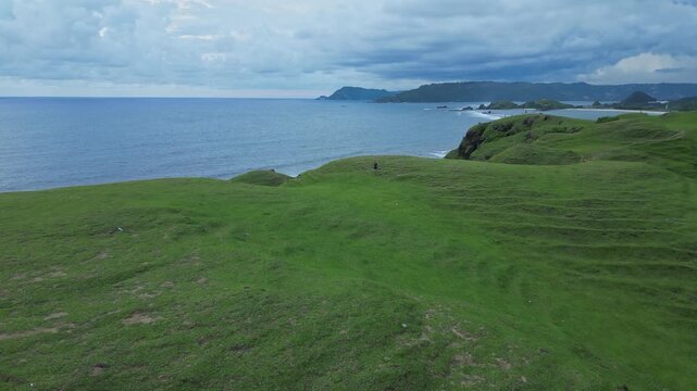 Woman Walking Ridge With Ocean View, Narrow Grassy Paths Snake Between Rolling Knolls Toward Distant Cove, Cinematic Composition With Moody Sea Horizon, Solitary Hike,Bukit Merese, Lombok, Tanjung Ann