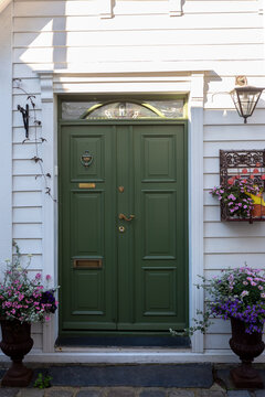 Vertical detailed view of a vintage olive green double entrance door on a white wooden building facade in Old Stavanger. Decorated with beautiful pink potted flowers on a wrought iron shelf.