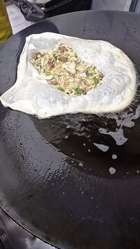 Street food vendor preparing traditional Indonesian martabak telur, filling thin dough with egg and green onion mixture then folding it on a flat griddle pan.
