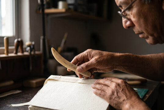 Close-up of senior artisan hands using a bone folder tool for bookbinding.