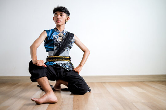 Young Indonesian Male Dancer Posing in Traditional Elegant Blue batik Costume on Light Background