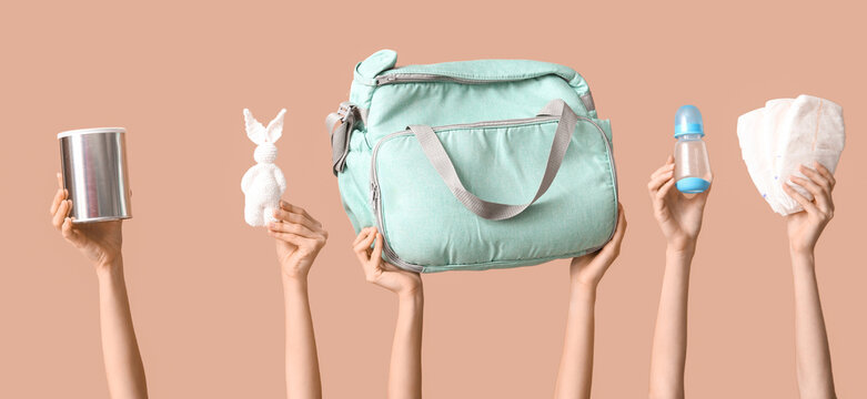 Hands holding baby essentials and diaper bag on beige background