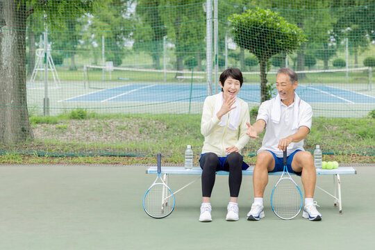 テニスの後にベンチで談笑するシニア夫婦
