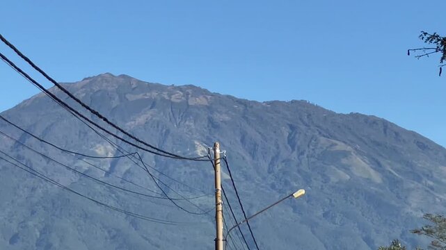 Morning view of the rural landscape in Magetan, East Java, Indonesia, featuring agricultural fields, a quiet village road, Mount Lawu, and the surrounding hills under a clear blue sky. The image depic