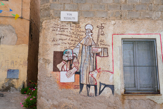 Stylized mural of Saint Anthony Abbot with a pig and a portrait of Antonio Gramsci on a building facade in Orgosolo, Barbagia, Sardinia, Italy