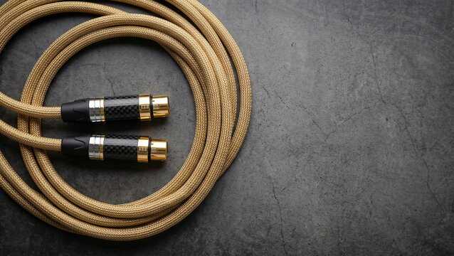 Audio cable coiled golden braided with XLR connectors on dark textured surface, for professional sound equipment or high-fidelity audio.