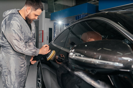 Worker polishing car with special grinder and wax from scratches at the car service station. Professional car detailing and maintenance concept