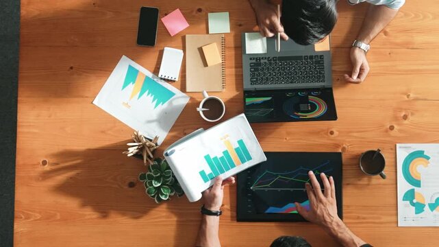 Male leader use laptop to analysis graph while marketing team working on tablet and looking at financial chart. Top view of startup group finding solution and planning strategy together. Convocation.