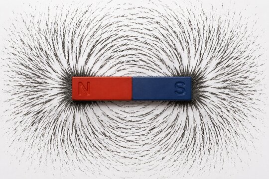 A bar magnet with iron filings showing curved magnetic field lines.
