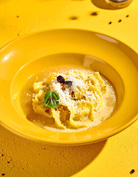 Gourmet cappelletti pasta in glossy broth with reggianito cheese on yellow background
