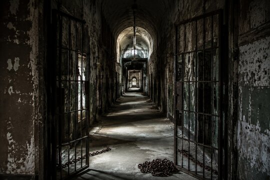 An empty prison corridor with open iron doors and chains on the floor.