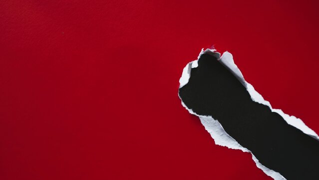 A bright red paper sheet with a large jagged hole revealing a dark black background.
