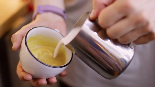 Garnishing drink. Pouring foamed milk. Barista hand adding frothing steaming creamy liquid to aromatic beverage serving coffee in ceramic cup.