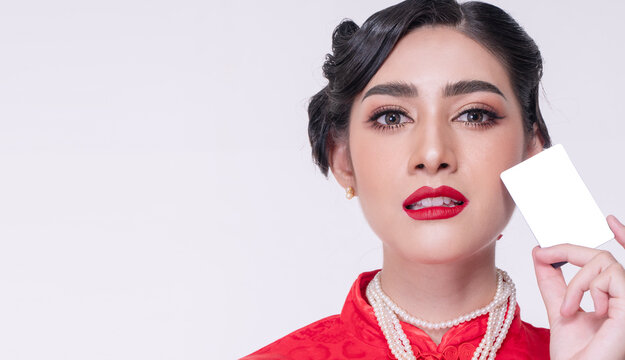 Close-up portrait of beautiful Asian woman in red traditional Chinese dress holding a blank white credit card near her face. Elegant female shopper on isolated white background with copy space.