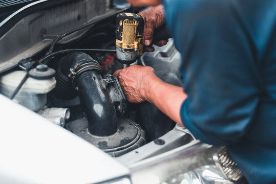 Close-up of mechanic's hands using a power tool to repair a car engine in an auto service workshop.