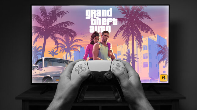 Grand Theft Auto VI sunset artwork on TV screen with PS5 DualSense controller showing Jason and Lucia by classic car and palm trees