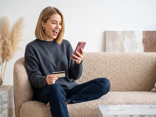Excited Young Woman Doing Online Shopping with Credit Card and Smartphone at Home, Happy Smiling Female Celebrating Success Transaction Sitting on Sofa in Cozy Living Room
