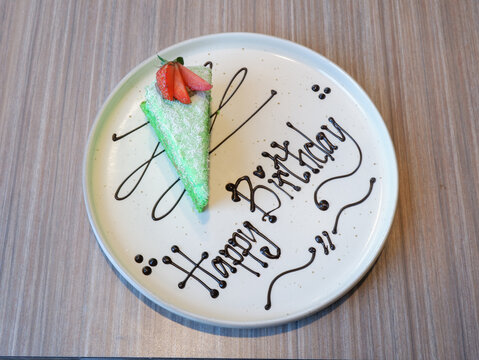 ​Pandan klepon cake slice with happy birthday chocolate writing on a white plate, celebration dessert serving close up