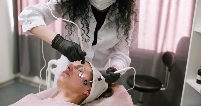 Cosmetologist salon. Lifting therapy. Female in black gloves using modern device for professional microcurrent face at spa workplace.
