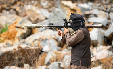 Fototapeta premium Armed militant aiming a rocket launcher during a simulated conflict scenario in rocky outdoor terrain