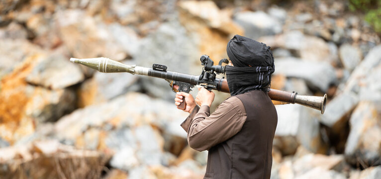 Armed militant aiming a rocket launcher during a simulated conflict scenario in rocky outdoor terrain