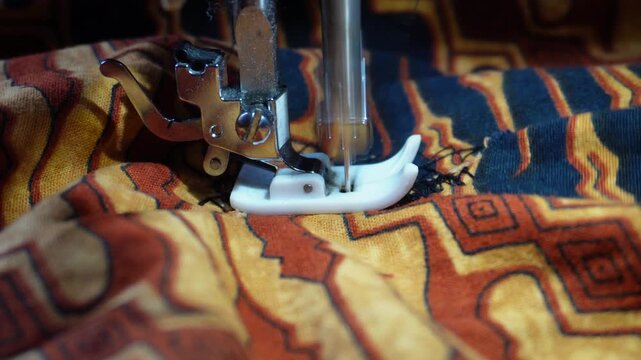 Close up of electric sewing machine foot stitching traditional batik patterned fabric with black thread