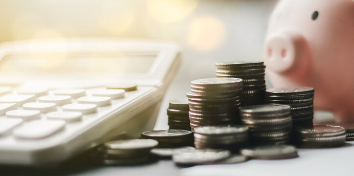 Pink piggy bank with stacks of coins and calculator on desk. Concept of financial planning, money saving, investment growth, retirement fund, and wealth management for business and individual.
