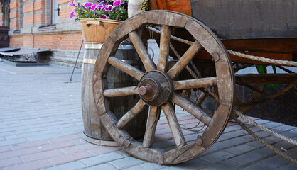 Obraz premium Close-up of an old wooden cart wheel set against the background of an outdoor building.