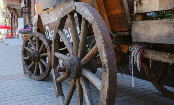 Close-up of an old wooden cart wheel set against the background of an outdoor building.