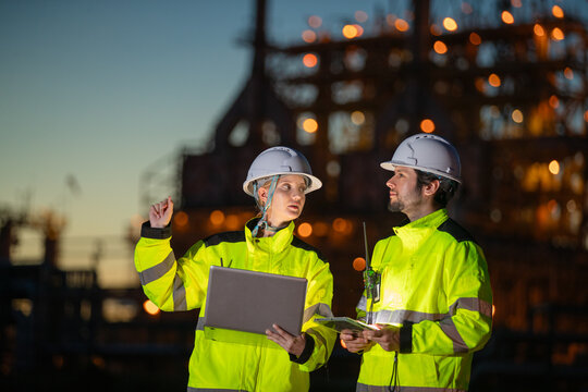 Engineers collaborating at oil and gas refinery during sunset discussing project plans with industrial background