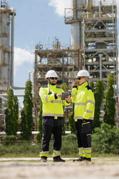 Engineers collaborating at an oil and gas refinery analyzing data on a tablet near industrial structures