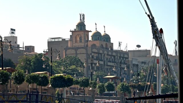 A daytime view of the Coptic Orthodox Cathedral of the Virgin Mary (Saint Mary's Church) rising above the tree-lined Nile Corniche promenade in Luxor, Egypt, showcasing its distinctive blue domes.
