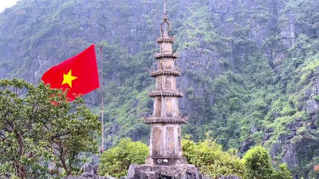 Static shot of Hang M&uacute;a Pagoda in Ninh Binh, Vietnam, with a Vietnamese flag waving in the wind atop Ngoa Long Mountain in the Trang An landscape.
