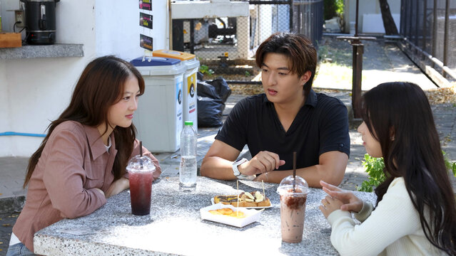 Three Asian University Students Talking Over Iced Drinks at Outdoor Cafeteria Table