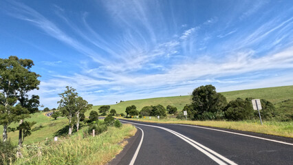 Naklejka premium Winding Country Road Through Green Hills Under Blue Sky in Armidale