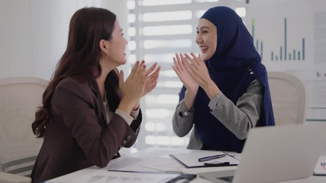 Two business colleagues celebrating success after reading great update on laptop at office desk