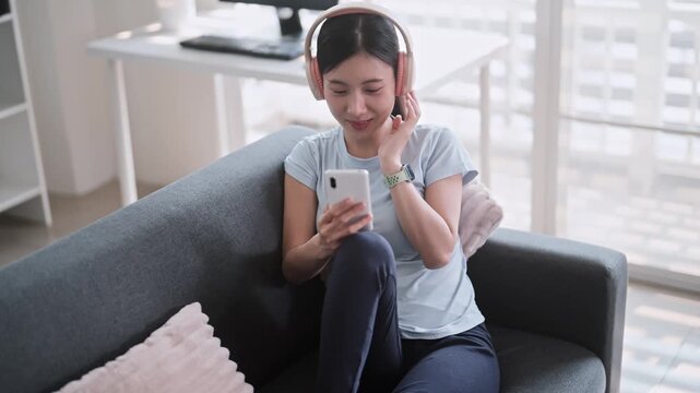 Asian woman in sports clothing using smartphone with headphones at home