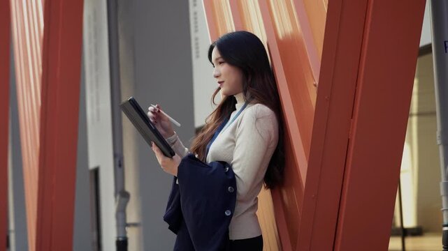 Asian business woman creates ideas and takes notes on a digital tablet outdoors in the city